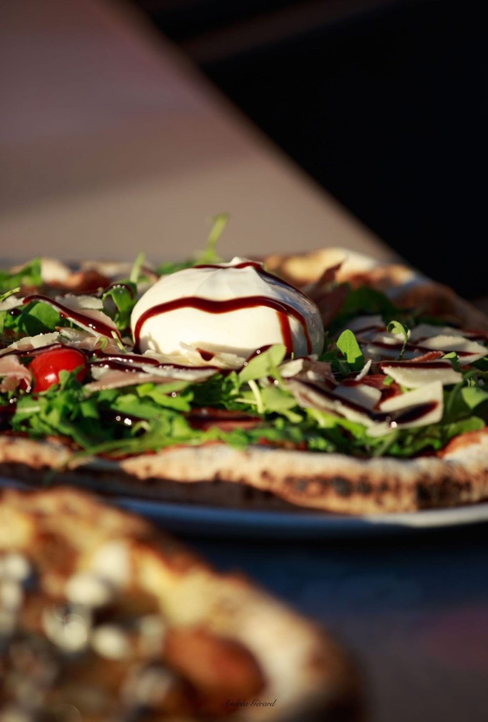Une pizza au feu de bois garnie de roquette et de burrata, avec un filet de crème balsamique